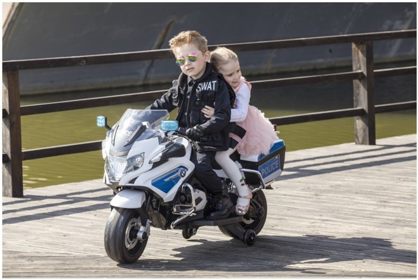 Two children play-acting as police officers on silver BMW electric ride on motorbike, wearing sunglasses
