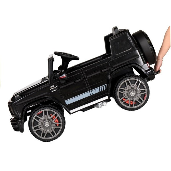 Person carrying a black Mercedes Benz G63 AMG electric ride-on car with shiny chrome rims for children.