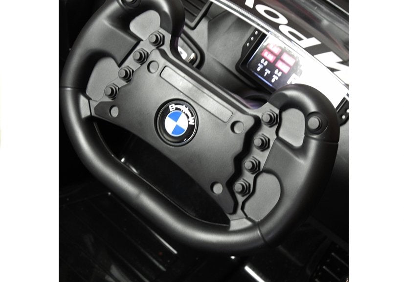 Black steering wheel inside a BMW M6 GT3 12 Volt electric ride-on car for kids, highlighting brand's logo.