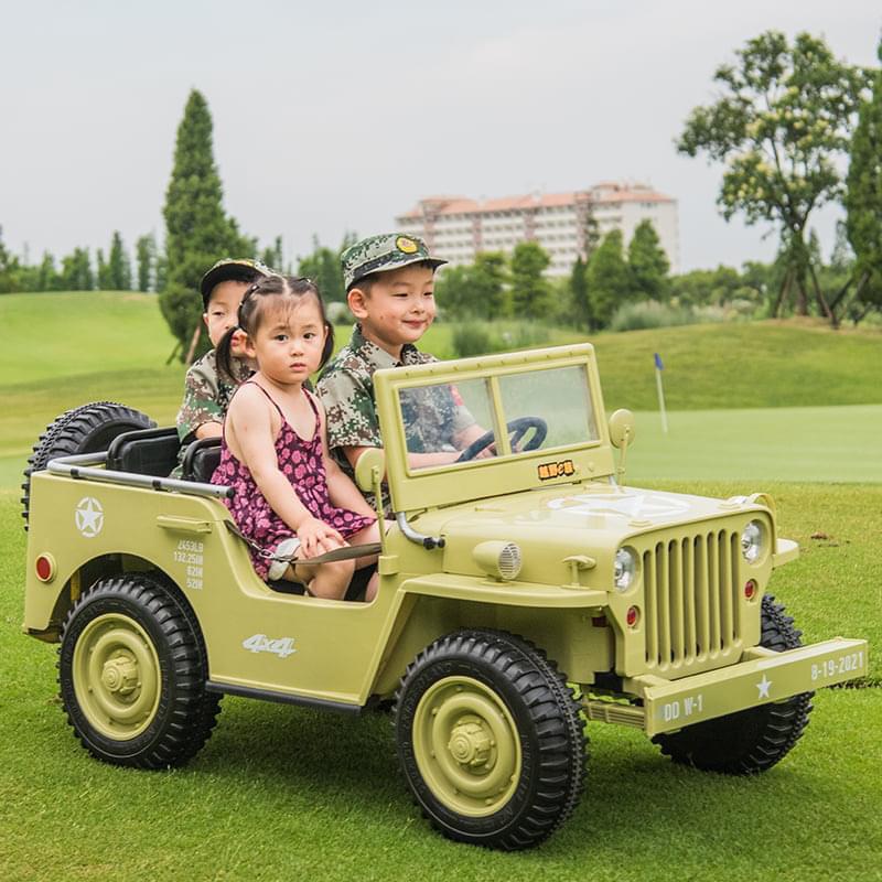 Children in camouflage outfits riding a 3-seater Willys Jeep electric ride on, khaki green color, outdoors on a grassy lawn.