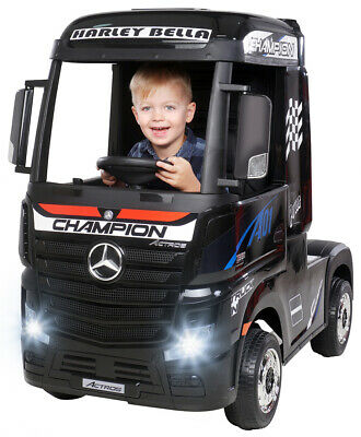Child smiling in black Mercedes Actros model ride-on lorry with 'champion' label.