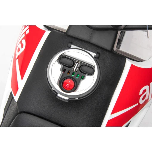 Close-up of Aprilia 12V electric motorbike for kids showing fuel tank cap and safety-related electronic controls.
