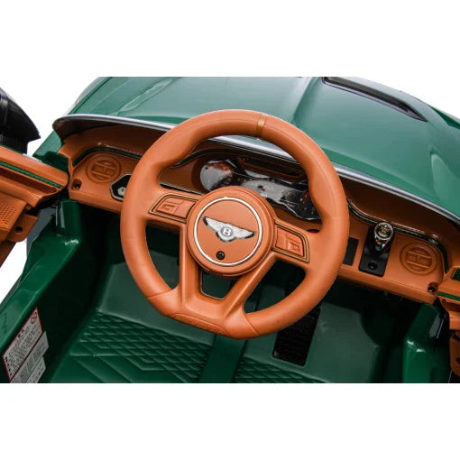 Close-up of green Blue Bentley Bacalar 12V electric ride on car's steering wheel and dashboard with woodgrain and orange details.