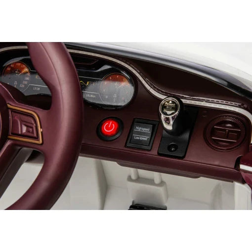 Interior view of a White Bentley Bacalar Electric Ride-On Car's dashboard, focusing on steering wheel and gauges for children.