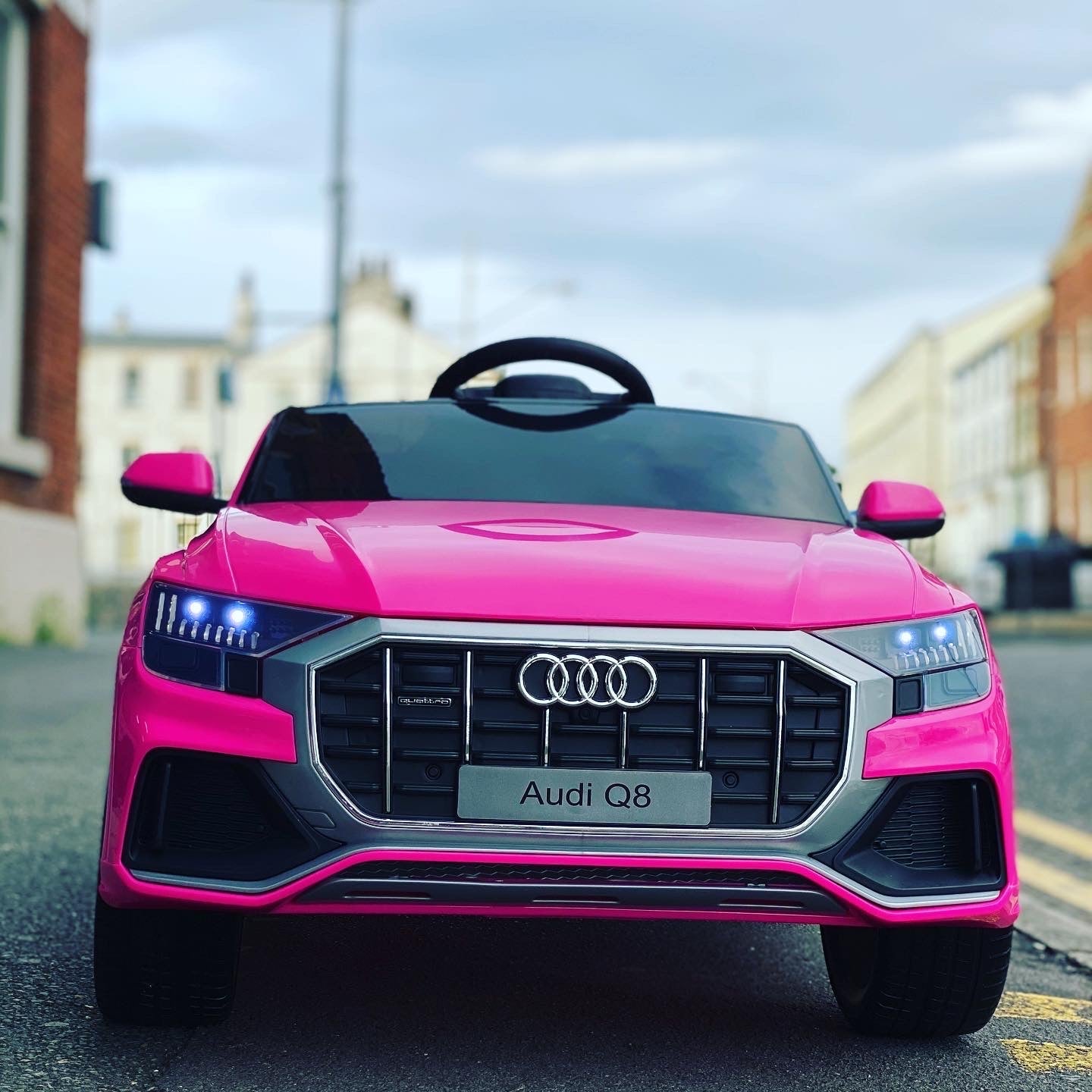 "Pink Audi Q8 SUV electric ride-on 12 Volt car for kids under parental remote control cruising on street"