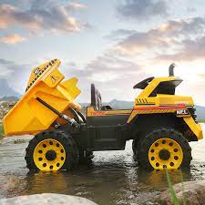 Two children enjoying a 12 Volt Electric Construction Truck ride on rocky terrain at dusk.