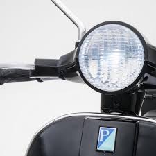 Close-up of a 12V black Vespa electric scooter's headlight and handlebar with parking permit sticker