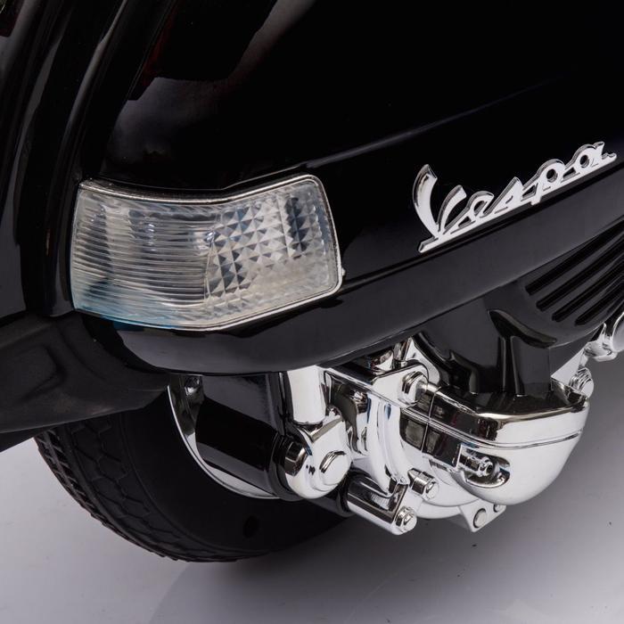 Close-up view of a black electric Vespa ride-on scooter for kids, displaying headlight and chrome details.